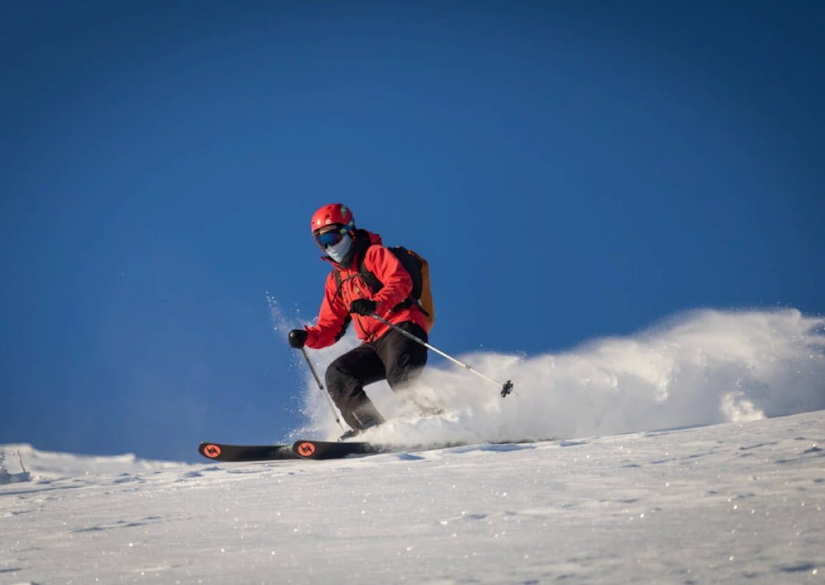 Skier in a red jacket carving through powder